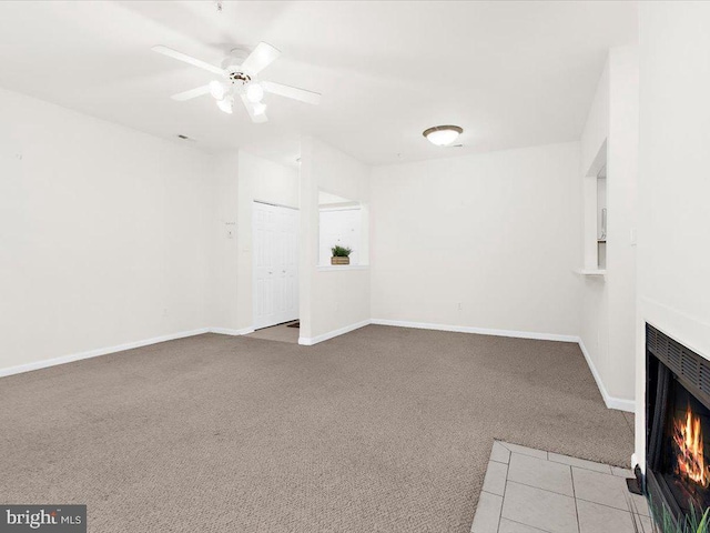 unfurnished living room with carpet, a fireplace with flush hearth, baseboards, and ceiling fan