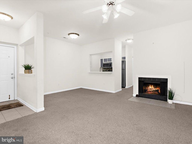 unfurnished living room featuring a fireplace with flush hearth, baseboards, ceiling fan, and carpet flooring