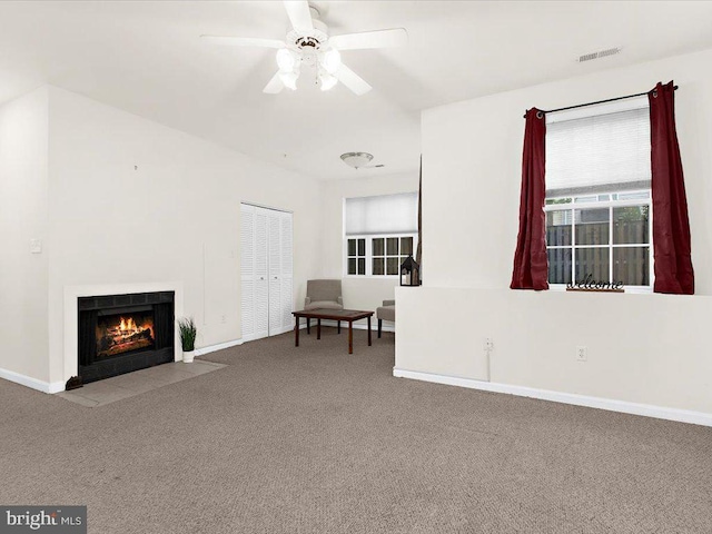 living area featuring visible vents, baseboards, a ceiling fan, a fireplace with flush hearth, and carpet flooring