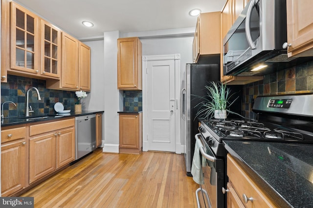 kitchen featuring light wood finished floors, tasteful backsplash, glass insert cabinets, stainless steel appliances, and a sink