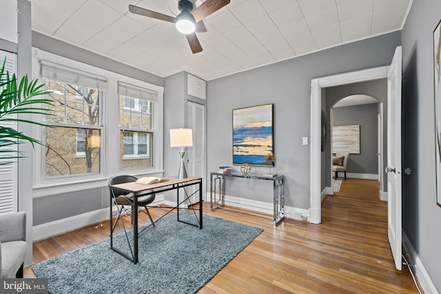 home office with baseboards, arched walkways, and wood finished floors