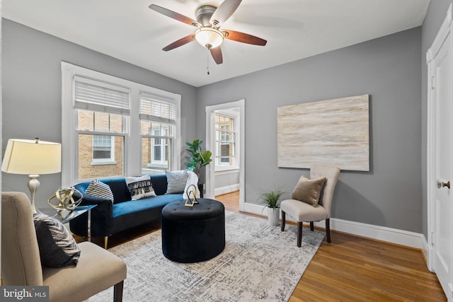 living room with ceiling fan, baseboards, and wood finished floors