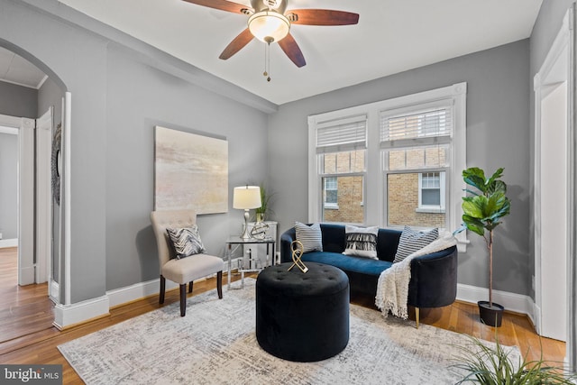 living area featuring arched walkways, wood finished floors, a ceiling fan, and baseboards