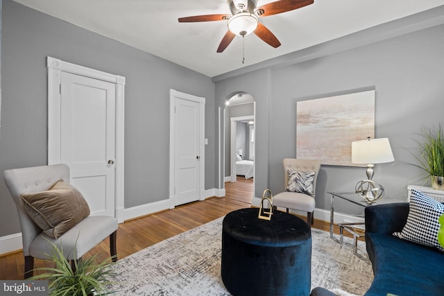 sitting room with baseboards, arched walkways, and wood finished floors