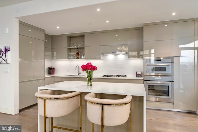 kitchen featuring a sink, gray cabinets, decorative backsplash, multiple ovens, and modern cabinets