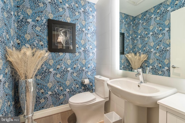 half bath with wood finished floors, toilet, and wallpapered walls