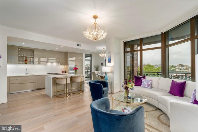 living area with visible vents, light wood-style floors, expansive windows, a chandelier, and baseboards