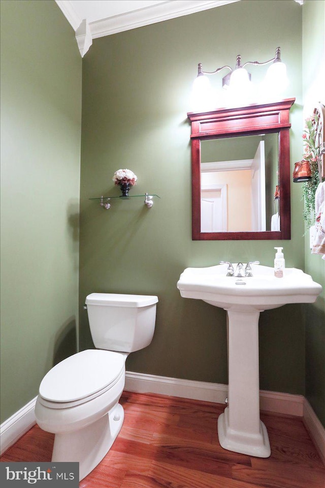 half bathroom featuring baseboards, wood finished floors, toilet, and crown molding