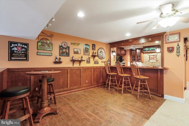 bar featuring a dry bar, a ceiling fan, wood finished floors, and wainscoting