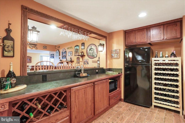 kitchen featuring wine cooler, brown cabinets, light wood finished floors, dark countertops, and black appliances