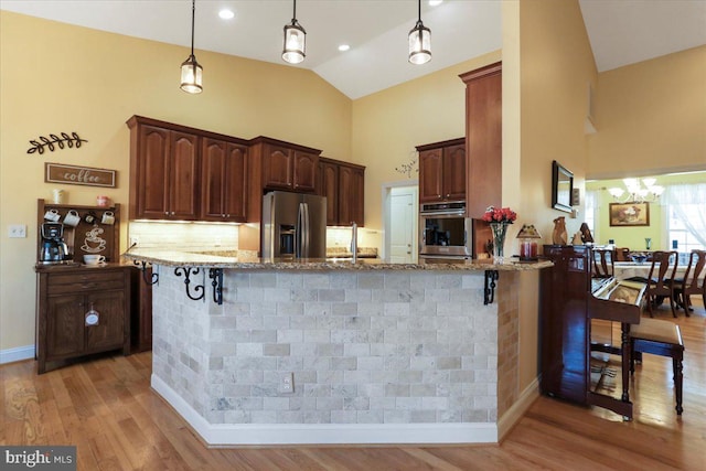 kitchen with light wood finished floors, a breakfast bar area, appliances with stainless steel finishes, and light stone counters