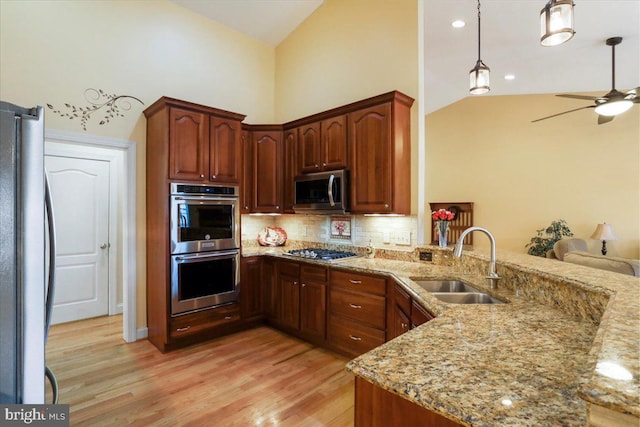 kitchen featuring stainless steel appliances, a sink, light wood-style flooring, and light stone counters