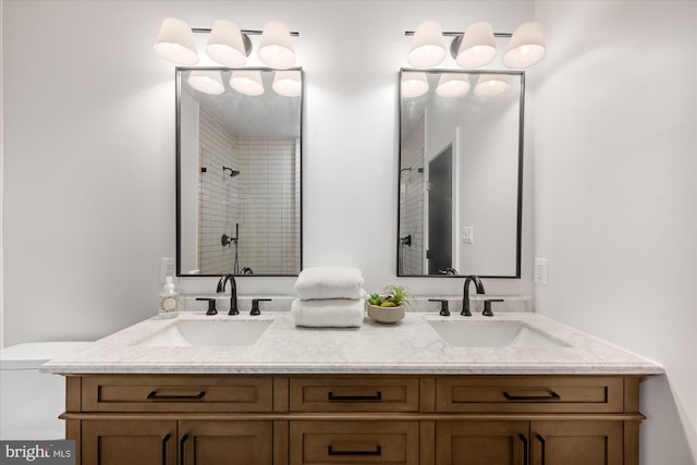 bathroom featuring double vanity, toilet, tiled shower, and a sink