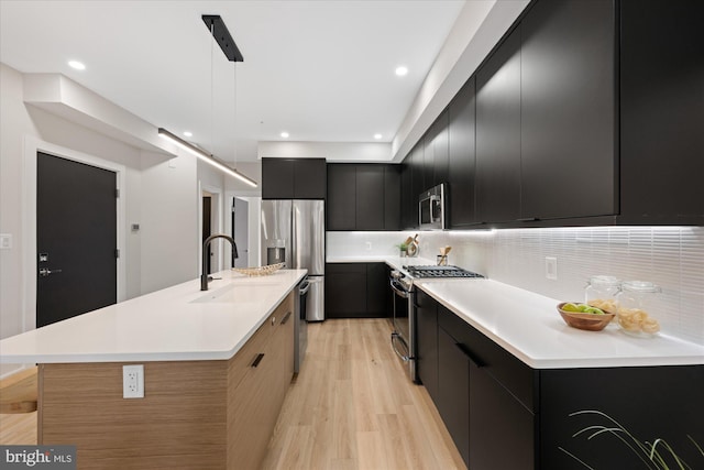 kitchen featuring a center island with sink, a sink, dark cabinetry, stainless steel appliances, and light countertops