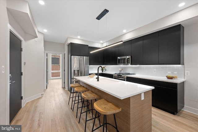 kitchen with a kitchen bar, modern cabinets, a sink, dark cabinetry, and appliances with stainless steel finishes