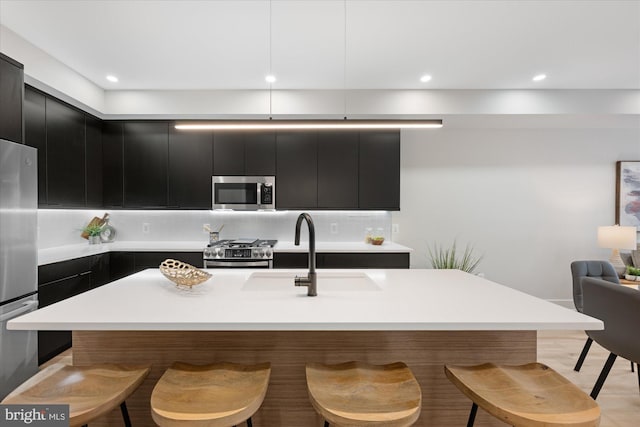 kitchen featuring dark cabinets, a kitchen bar, decorative backsplash, stainless steel appliances, and a sink