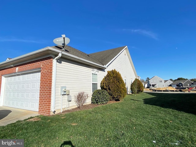 view of side of home featuring brick siding, a yard, driveway, and an attached garage