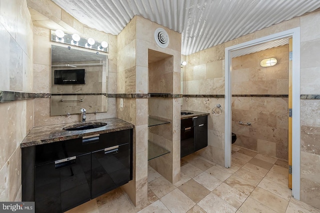 full bathroom featuring a sink, two vanities, and tile walls