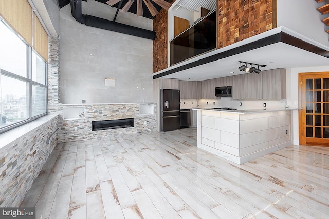 kitchen with a towering ceiling, light wood-type flooring, light countertops, and black fridge with ice dispenser