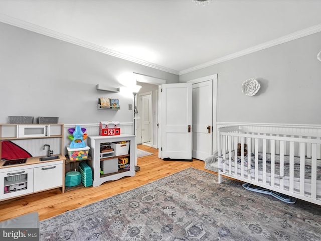 bedroom with light wood-type flooring, a nursery area, and crown molding