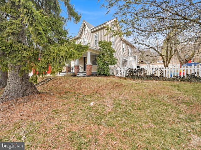 view of side of home with a yard, brick siding, covered porch, and fence