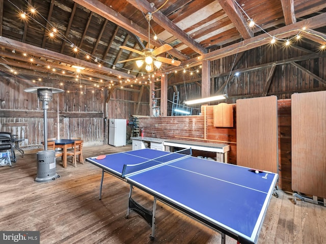 rec room with a ceiling fan, wood walls, wood-type flooring, and high vaulted ceiling