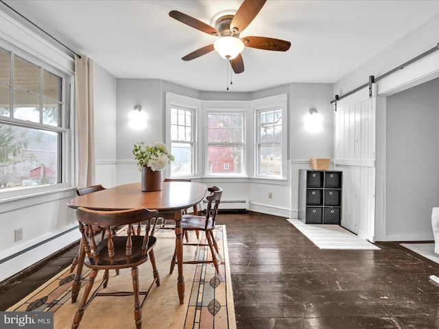 dining room featuring a baseboard heating unit, ceiling fan, baseboards, a barn door, and hardwood / wood-style floors