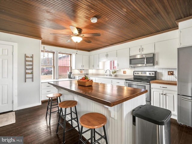 kitchen featuring dark wood-type flooring, butcher block counters, appliances with stainless steel finishes, white cabinets, and a sink