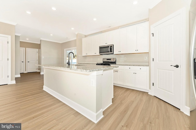 kitchen with stainless steel appliances, white cabinetry, a sink, an island with sink, and light wood-type flooring