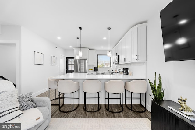 kitchen with a breakfast bar area, a peninsula, white cabinetry, freestanding refrigerator, and dark wood-style floors