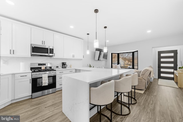 kitchen with white cabinets, appliances with stainless steel finishes, a breakfast bar, light countertops, and light wood-style floors