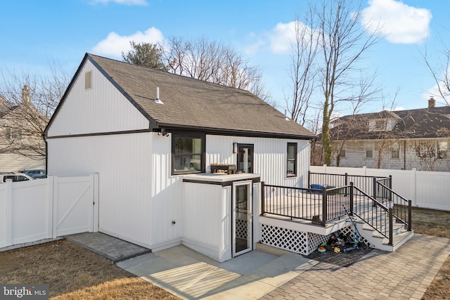 rear view of property featuring a shingled roof, a gate, a fenced backyard, and a deck