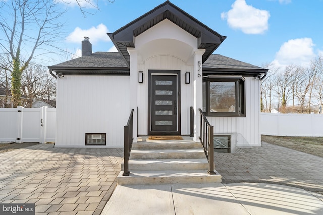 doorway to property with a gate, roof with shingles, fence, and a chimney