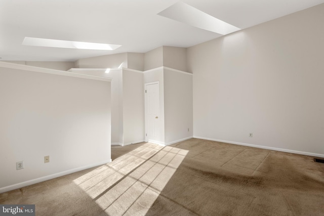 carpeted spare room featuring vaulted ceiling with skylight, visible vents, and baseboards