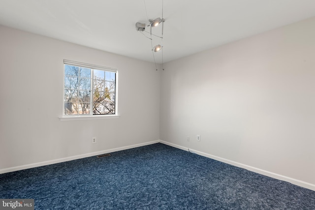 empty room with visible vents, dark carpet, and baseboards