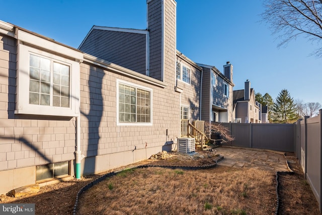 view of home's exterior featuring a patio area, a fenced backyard, a chimney, and central AC unit