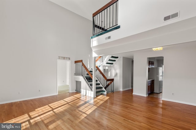 unfurnished living room featuring visible vents, a towering ceiling, stairway, wood finished floors, and baseboards