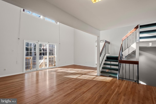 unfurnished living room featuring stairs, baseboards, and wood finished floors