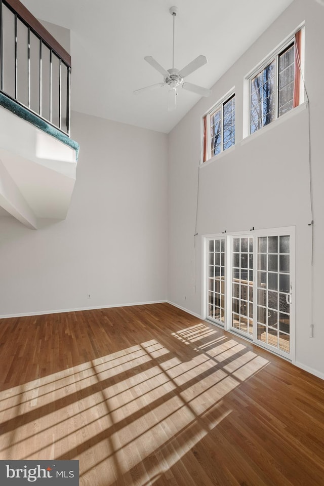 empty room with ceiling fan, wood finished floors, a towering ceiling, and baseboards