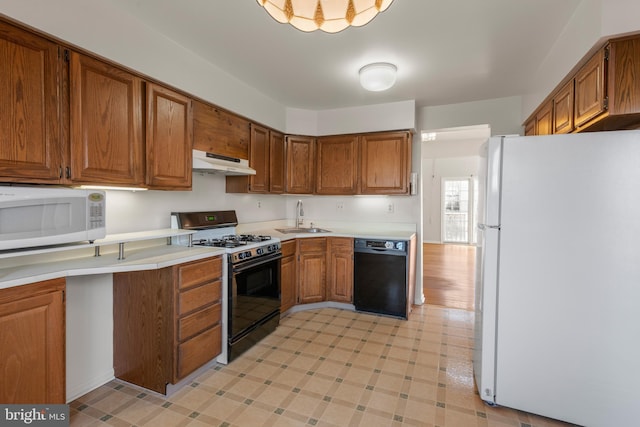 kitchen featuring under cabinet range hood, white appliances, a sink, light countertops, and brown cabinets