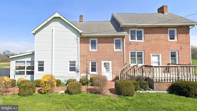 back of house with brick siding, a shingled roof, a yard, a wooden deck, and a chimney