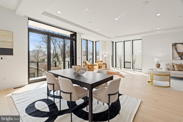 dining area with light wood finished floors, a tray ceiling, recessed lighting, and a healthy amount of sunlight