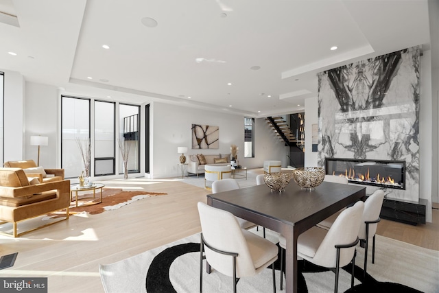 dining room with a high end fireplace, stairway, wood finished floors, a tray ceiling, and recessed lighting