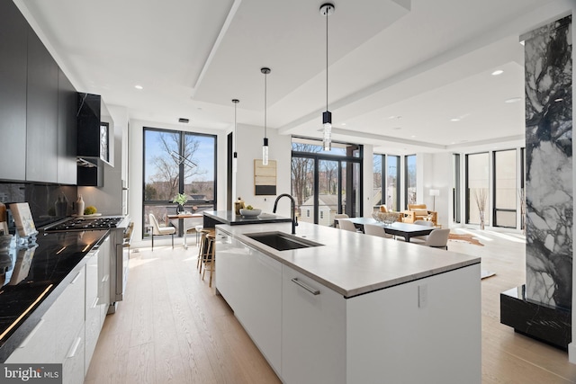 kitchen with light wood-style flooring, modern cabinets, open floor plan, high end stainless steel range, and a sink