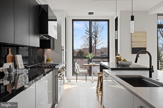 kitchen with stainless steel stove, hanging light fixtures, light wood-style floors, a sink, and modern cabinets