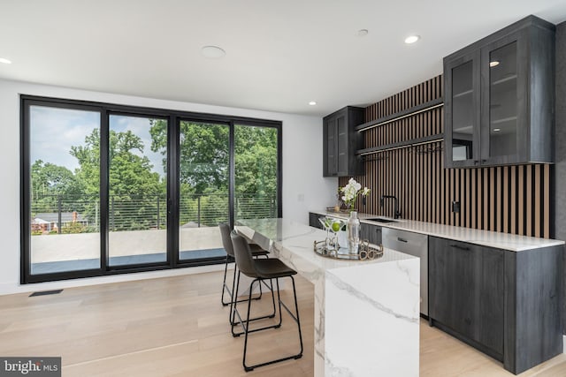 kitchen with dishwasher, glass insert cabinets, a center island, light stone countertops, and light wood-type flooring