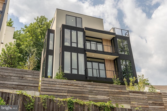 rear view of property with a balcony, fence, and stucco siding