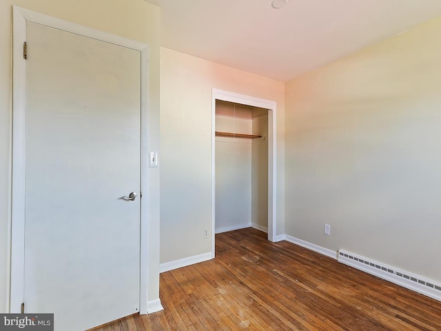 unfurnished bedroom featuring a closet, a baseboard radiator, wood-type flooring, and baseboards