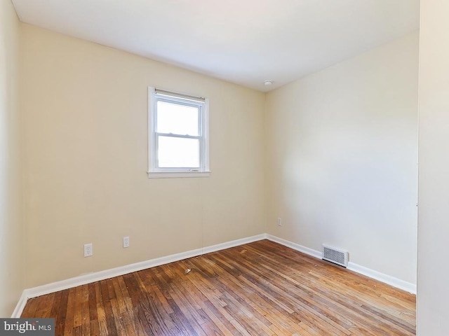 unfurnished room featuring baseboards, visible vents, and hardwood / wood-style floors