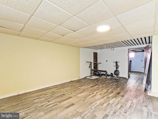 workout room featuring a paneled ceiling, light wood-style floors, and baseboards